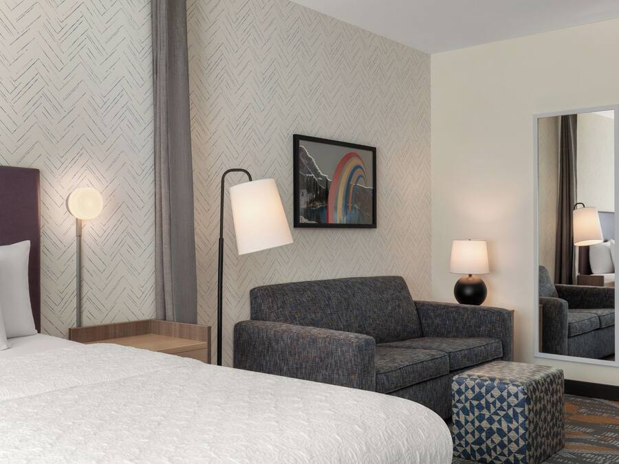 Una habitación de hotel con una cama, un sofá, un pequeño taburete, un escritorio y un espejo.