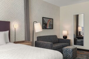 Una habitación de hotel con una cama, un sofá, un pequeño taburete, un escritorio y un espejo.