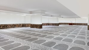 Un espacio interior amplio con piso estampado, paredes blancas y un atril a lo lejos.