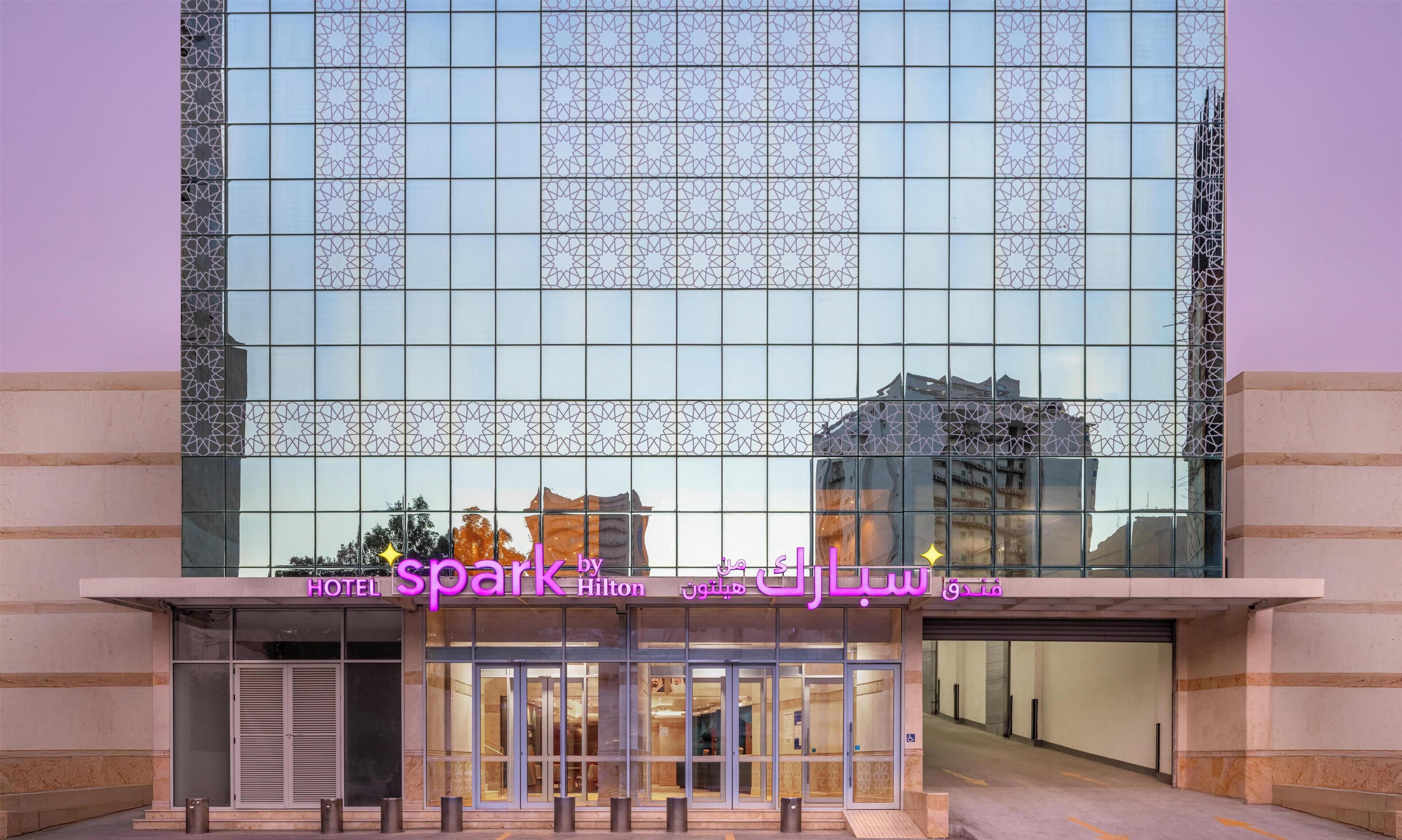 A hotel entrance with a modern glass facade, a visible entrance, and a sign indicating it's a Hilton hotel.
