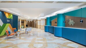 Vestíbulo de hotel con mostrador de recepción, zona de estar y suelo con estampado geométrico.