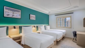 Habitación de hotel con tres camas, un escritorio, una silla y una ventana con vista a edificios.