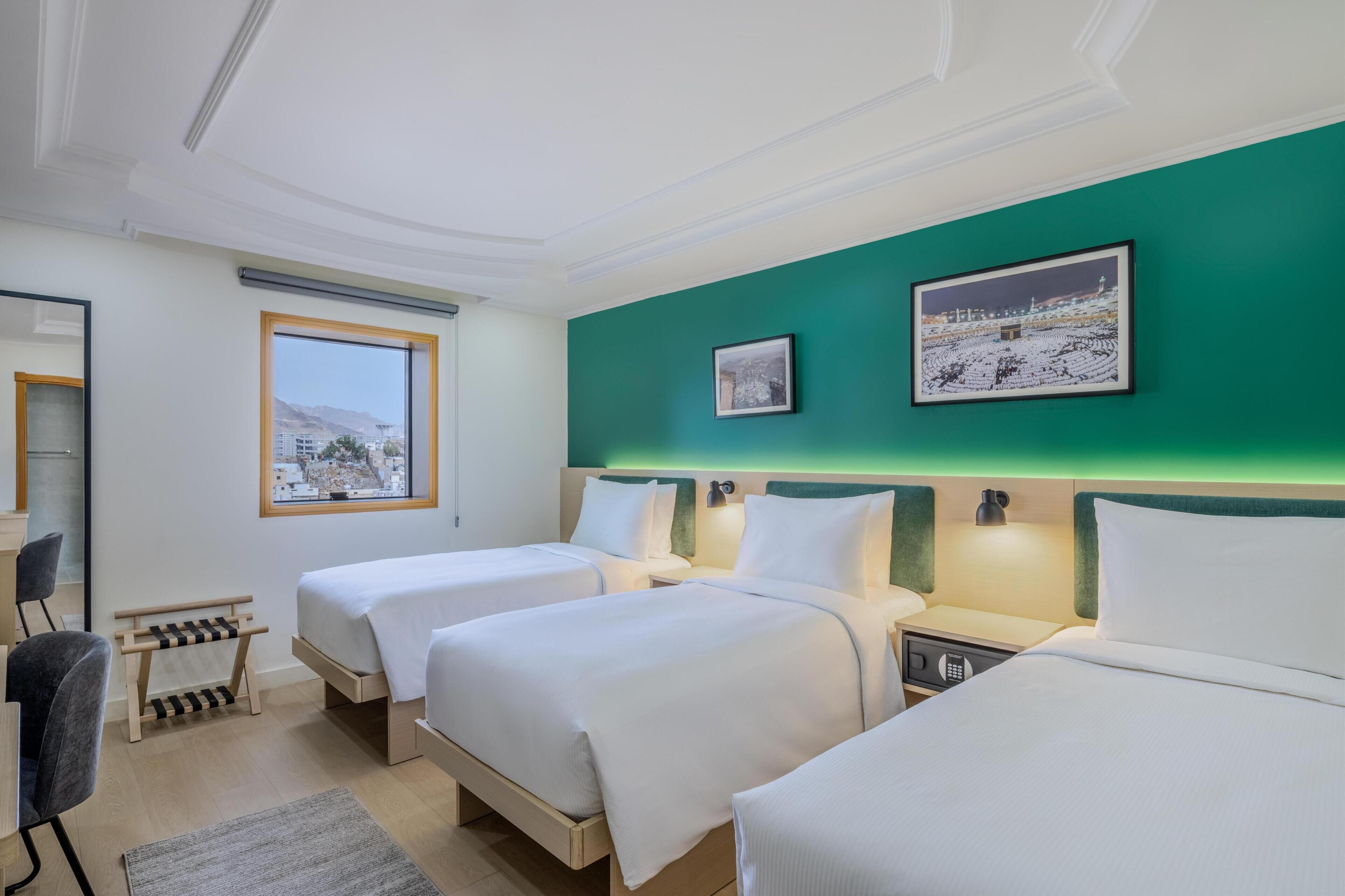 Une chambre d’hôtel avec deux lits, un bureau, une chaise, une fenêtre donnant sur un beau paysage et des œuvres d’art accrochées au mur.