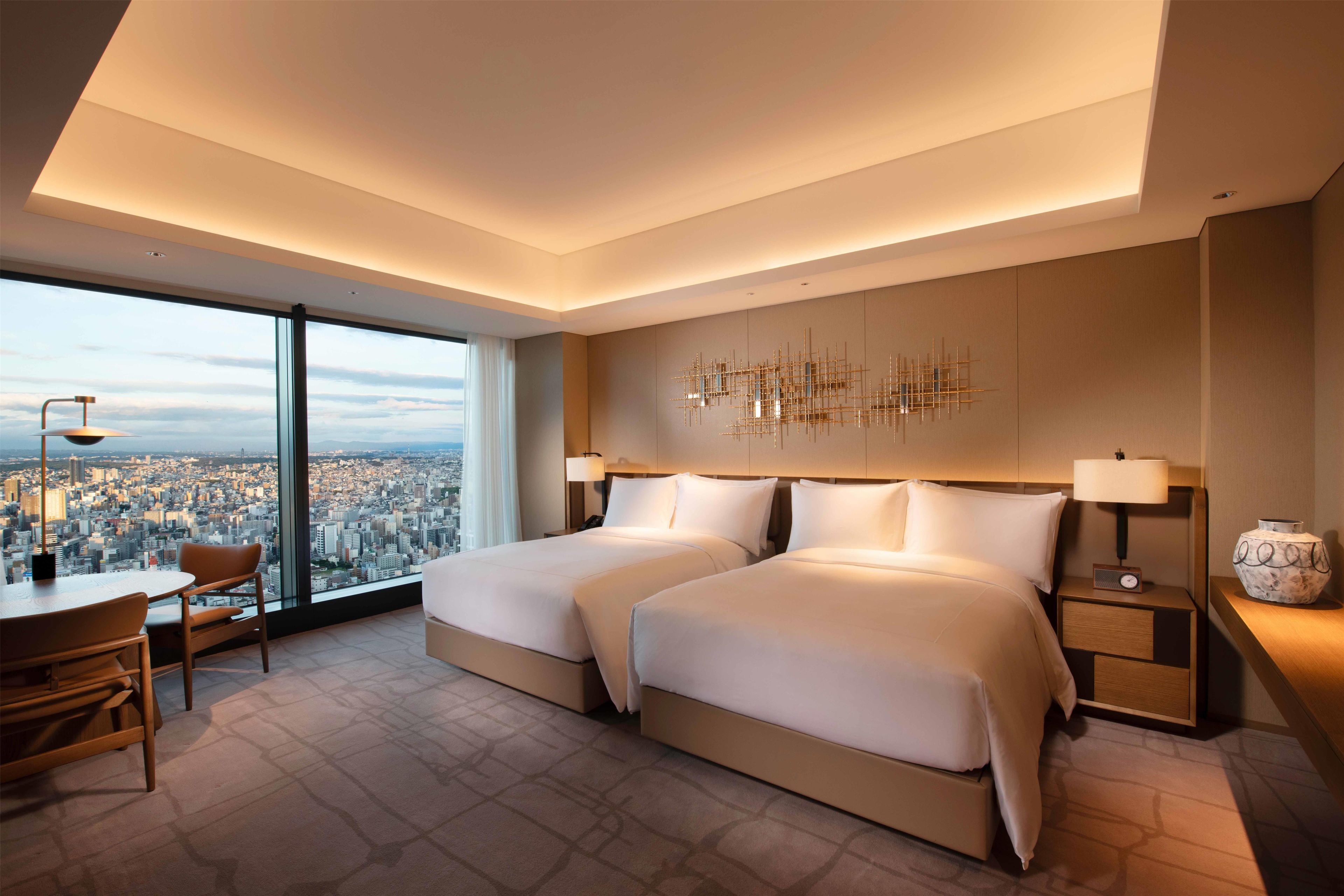 Habitación de hotel moderna con dos camas, vistas a la ciudad, un área de comedor y un adorno decorativo en la pared.