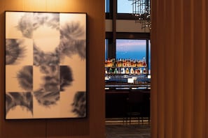 A bar area with a view of the sea through large windows, a bar counter with various bottles, and a chair. - Conrad Nagoya (Nagoya)