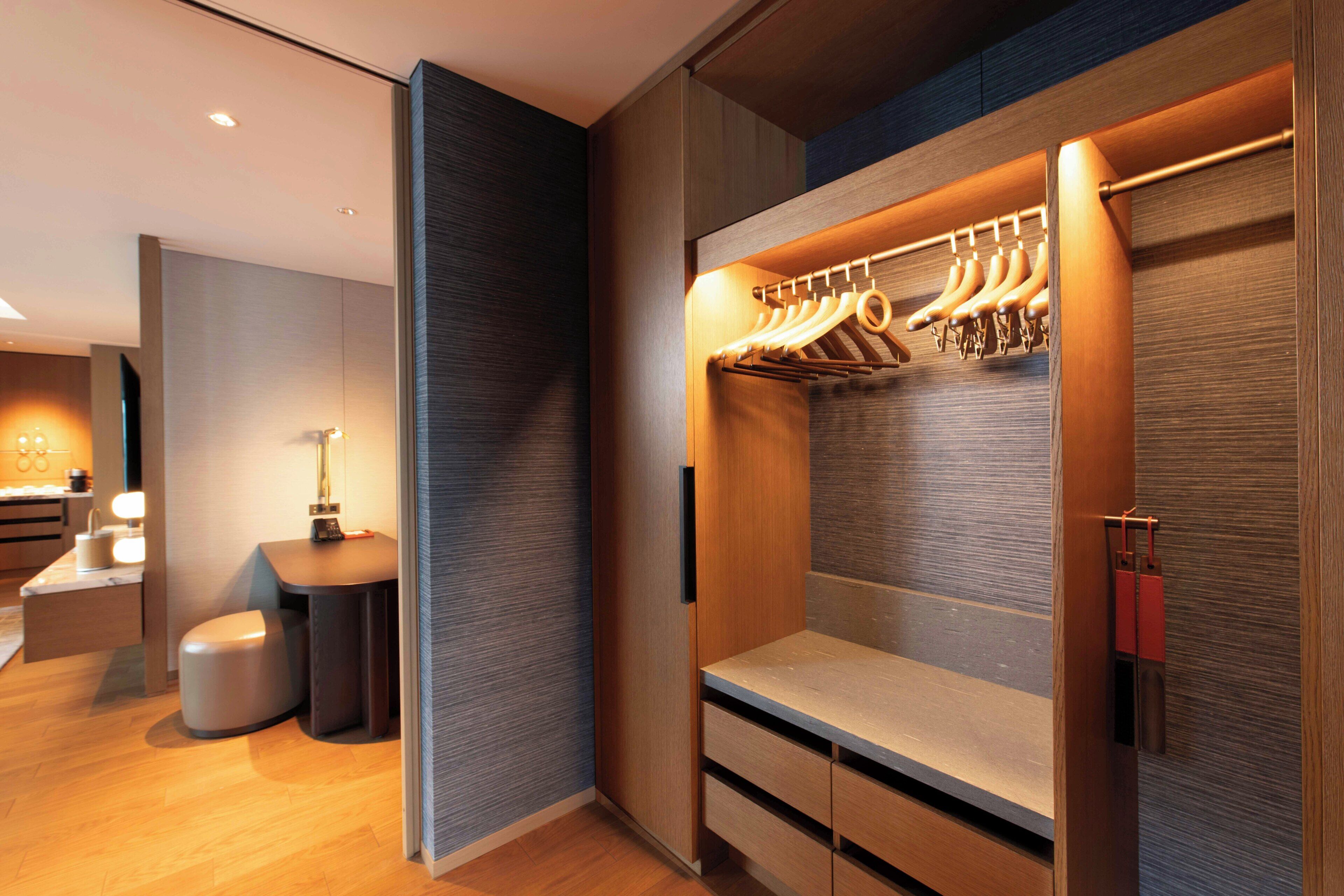 Une chambre d’hôtel moderne dotée d’un placard intégré, d’un petit coin salon et d’un bureau avec une lampe.