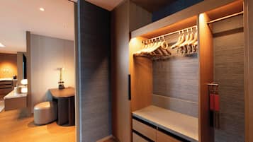 Une chambre d’hôtel moderne dotée d’un placard intégré, d’un petit coin salon et d’un bureau avec une lampe.