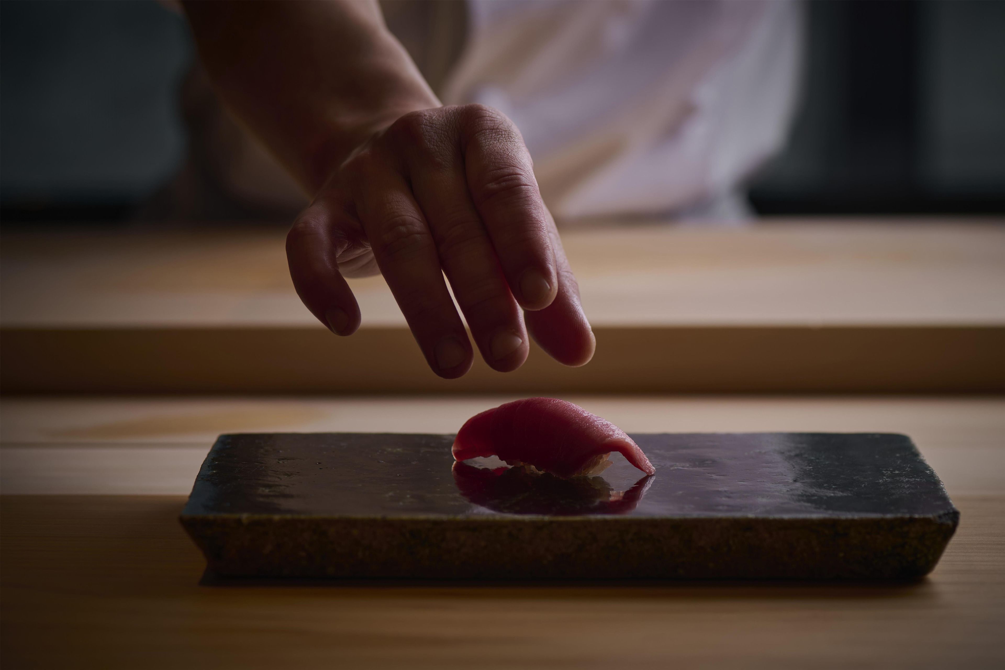 A hand placing a red object on a dark rectangular surface.