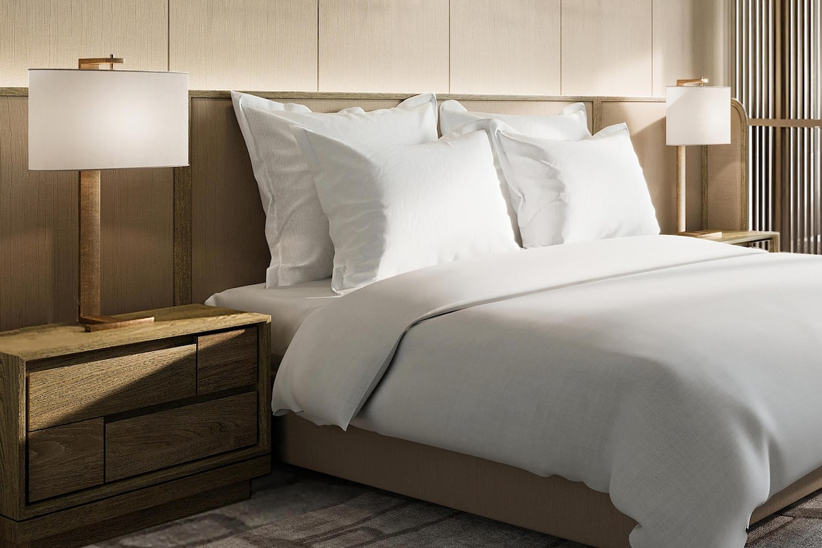 A neatly made bed with white linens, two bedside lamps, and a wooden nightstand with drawers.