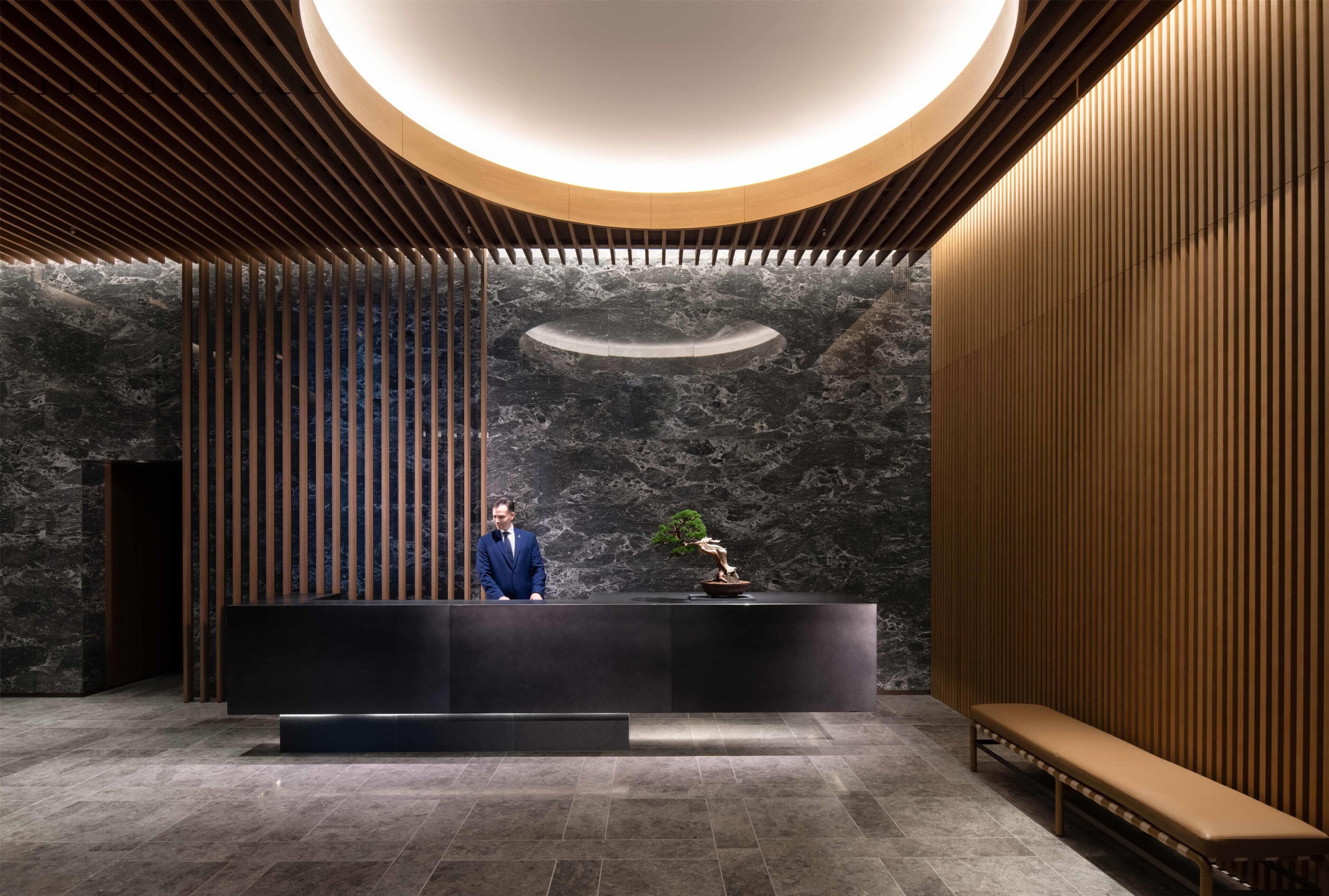 A reception area with a modern design, featuring a reception desk, a bench, and a large circular light fixture.