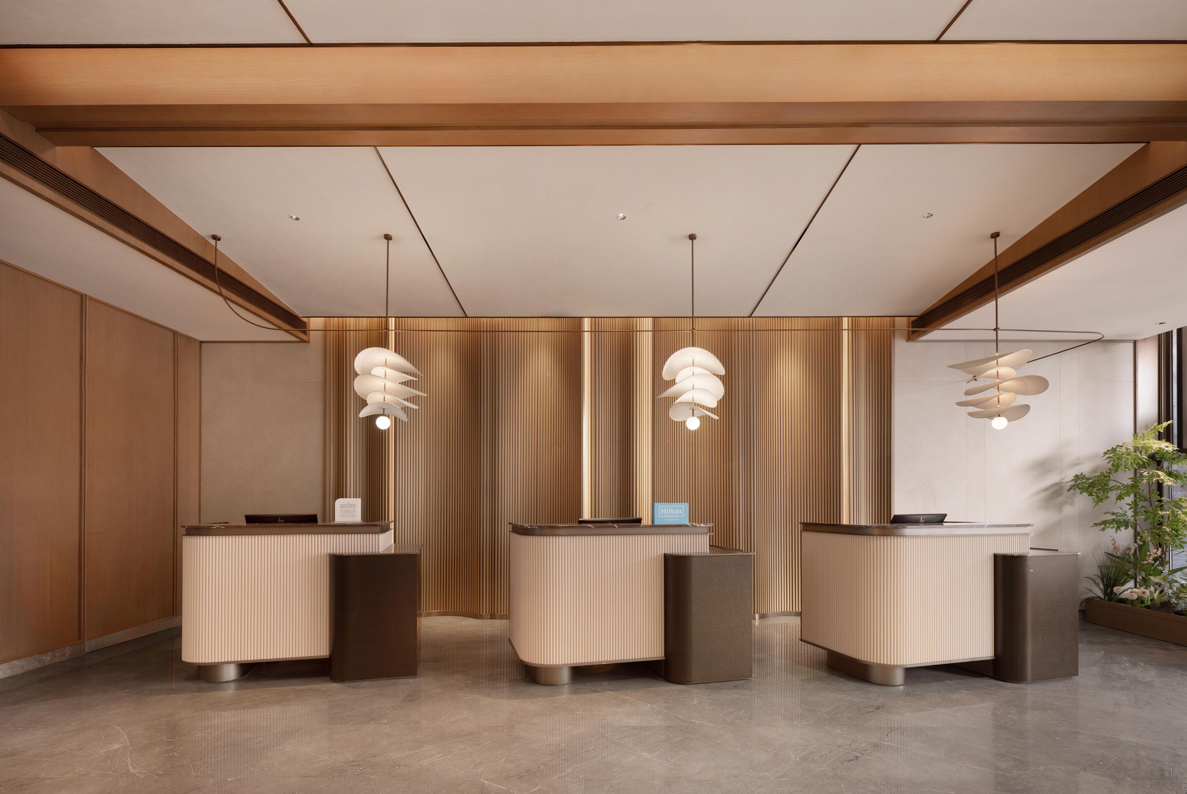 A modern hotel reception area with three reception desks, a wooden ceiling, and pendant lighting.
