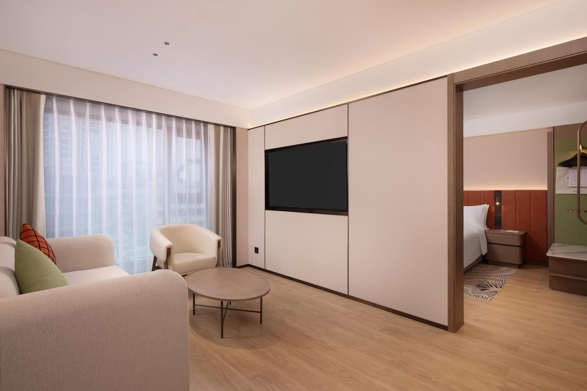 Una habitación de hotel moderna con sofá, sillón, televisor de pantalla plana y cama con mesita de noche.