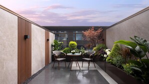 A modern outdoor seating area with a table and chairs, surrounded by plants and a view of a building. - Hilton Garden Inn Chengdu Huaxi Wuhou Shrine (Nanchong)