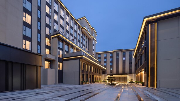 A modern hotel with a central courtyard, multiple floors, and a well-lit entrance. - Hilton Garden Inn Chengdu Huaxi Wuhou Shrine (Nanchong)