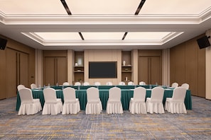 Une salle de conférence avec une longue table, des chaises blanches et un grand écran.