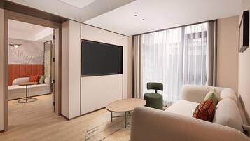 A modern hotel room with a flat-screen TV, a sofa, a small table, and a view of the city through large windows.
