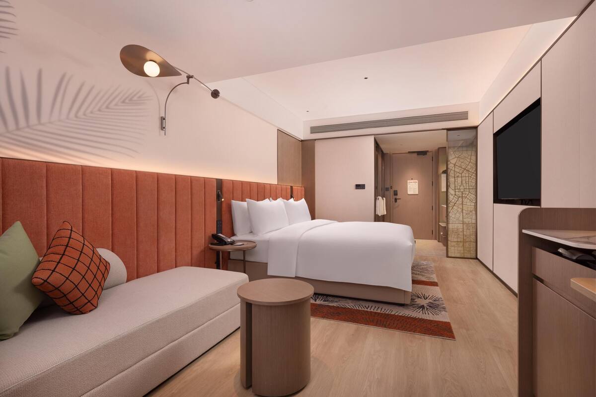 Una habitación de hotel moderna con cama, sofá, una pequeña mesa redonda, lámpara y televisor.