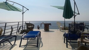 Terraza con mobiliario exterior, incluyendo sillas y una mesa, con vista a un cuerpo de agua.