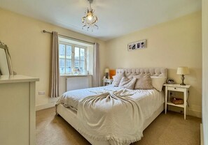Un dormitorio con cama, mesitas de noche, lámpara, radiador y ventana con cortinas.