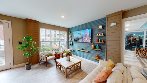 Ein geräumiges Wohnzimmer mit großem Fenster, einem Blumentopf, einem Couchtisch aus Holz, einer Couch und einem an der Wand befestigten Fernseher.