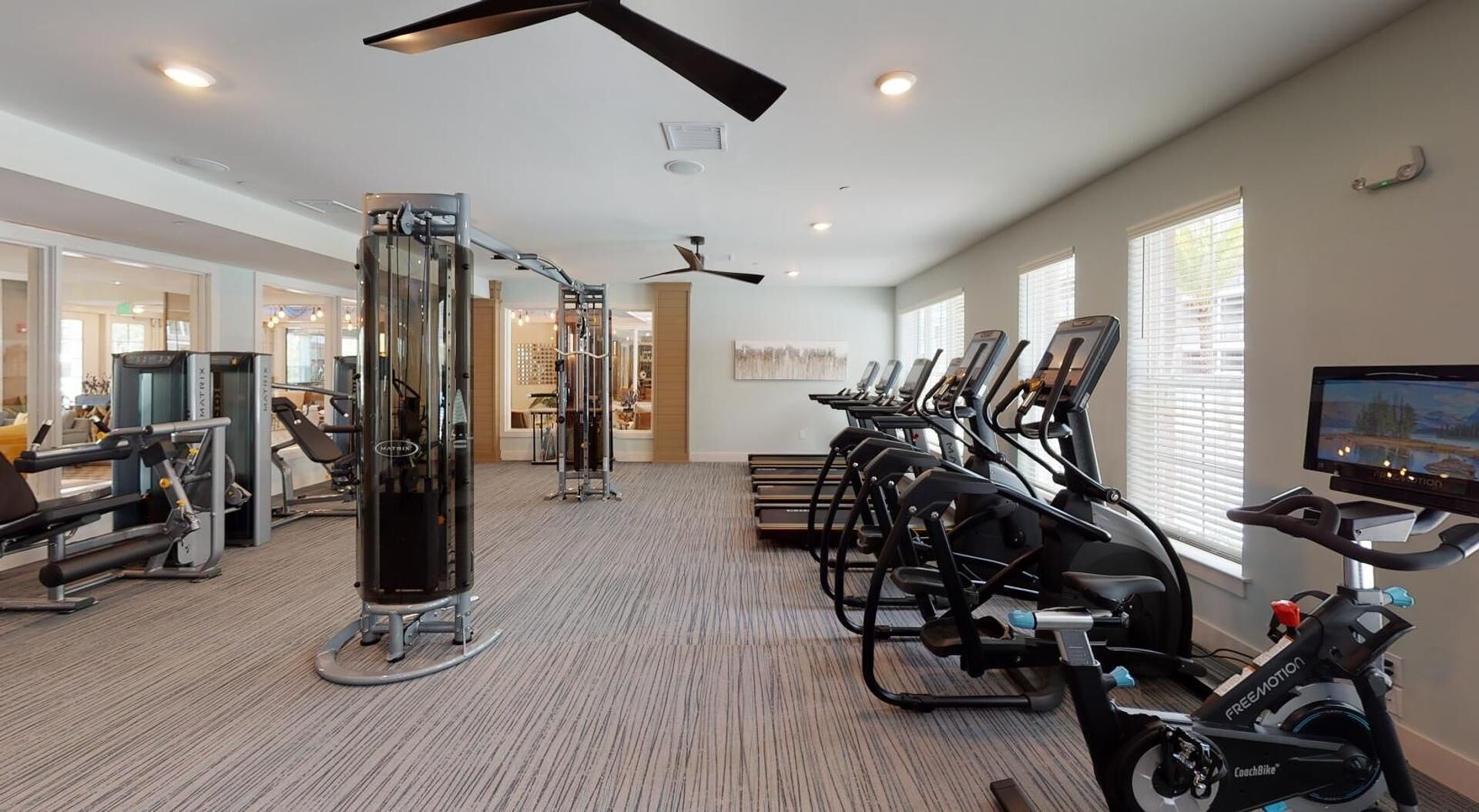 A gym with cardio machines, weight equipment, and a TV screen.