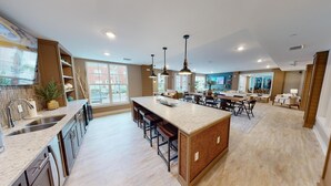 A spacious kitchen with a central island, modern pendant lighting, and a view of the outside through large windows. - Landing | Spectacular 2BD, Gym, Game Room (Orlando)