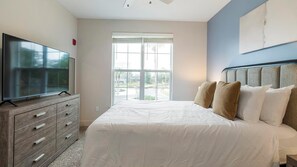 A bedroom with a large bed, a TV on a wooden dresser, and a window with a view of the outdoors. - Landing | Amazing 1BD, Gym, Game Room (Orlando)