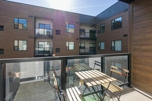 Un bâtiment moderne doté d’un balcon en verre, de meubles en bois et de nombreuses fenêtres.