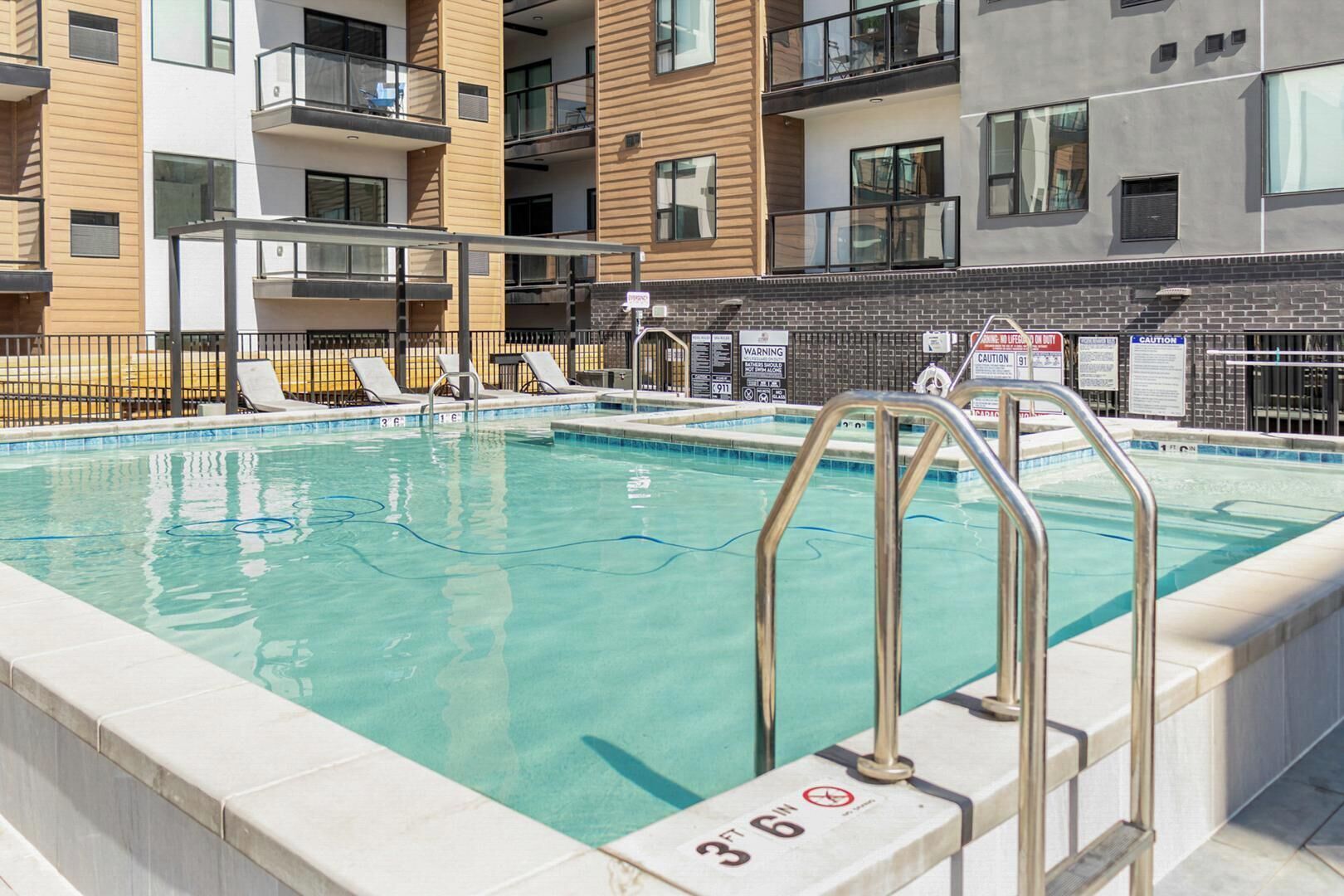 En swimmingpool med en djupmarkering som visar 1,07 meter (3 fot och 6 tum), omgiven av ett staket, och i bakgrunden syns en byggnad med balkonger och en fasad av tegel.