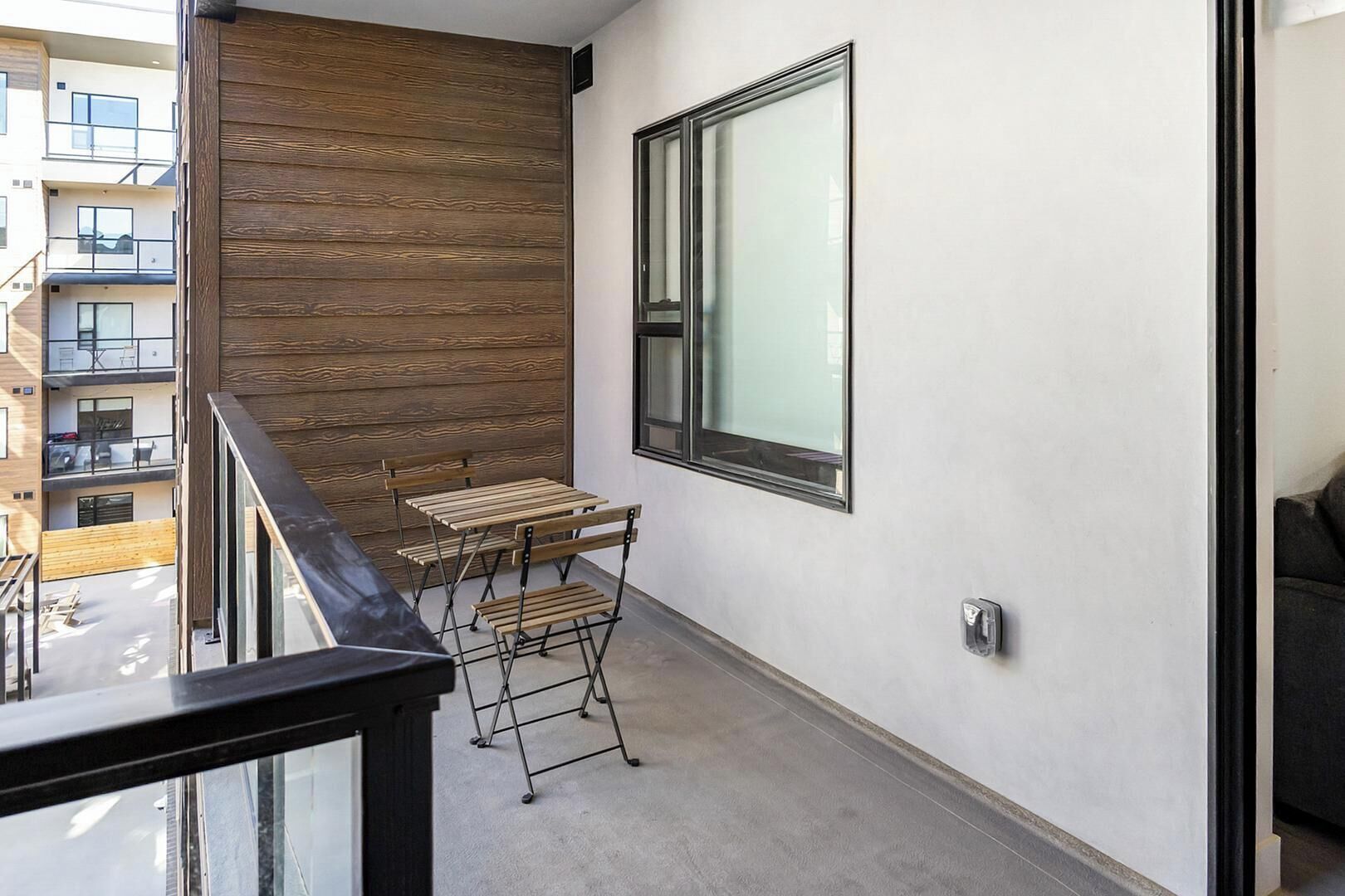 A balcony with a wooden wall, a window, and a table with chairs.