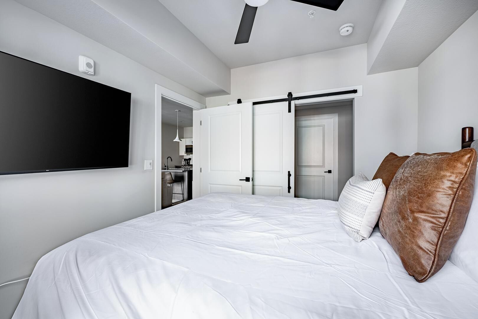 Et moderne hotelværelse med en stor seng, et fladskærms-tv, et skab med skydedøre og et tekøkken.