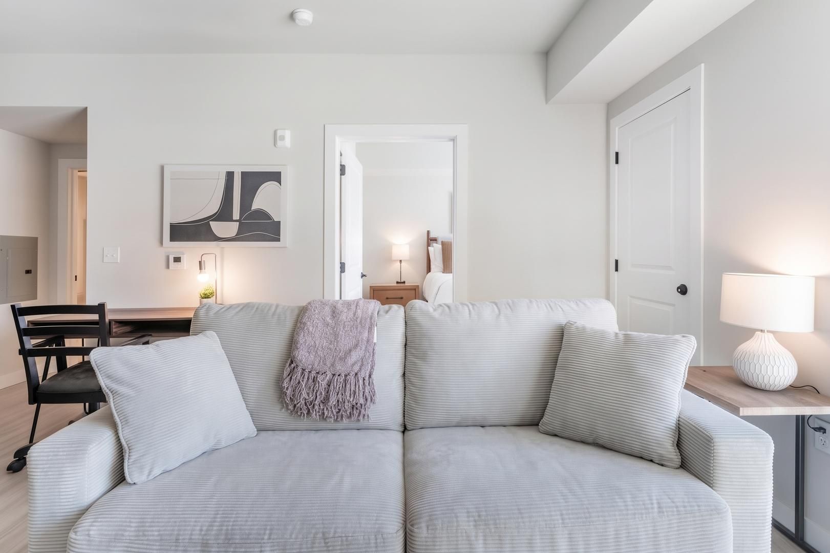 Een moderne woonkamer met een grijze bank, een eettafel en een lamp.
