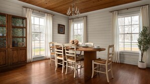Une salle à manger avec une table et des chaises en bois, de grandes fenêtres et un lustre.