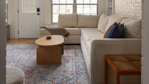 Un salon chaleureux, aménagé dans un style industriel, avec une grande fenêtre, un canapé, une table basse et un tapis à motifs.