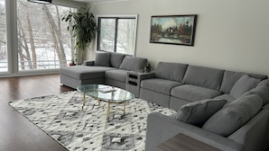 Ein modernes Wohnzimmer mit einem grauen Ecksofa, einem Glastisch und einem gemusterten Teppich.