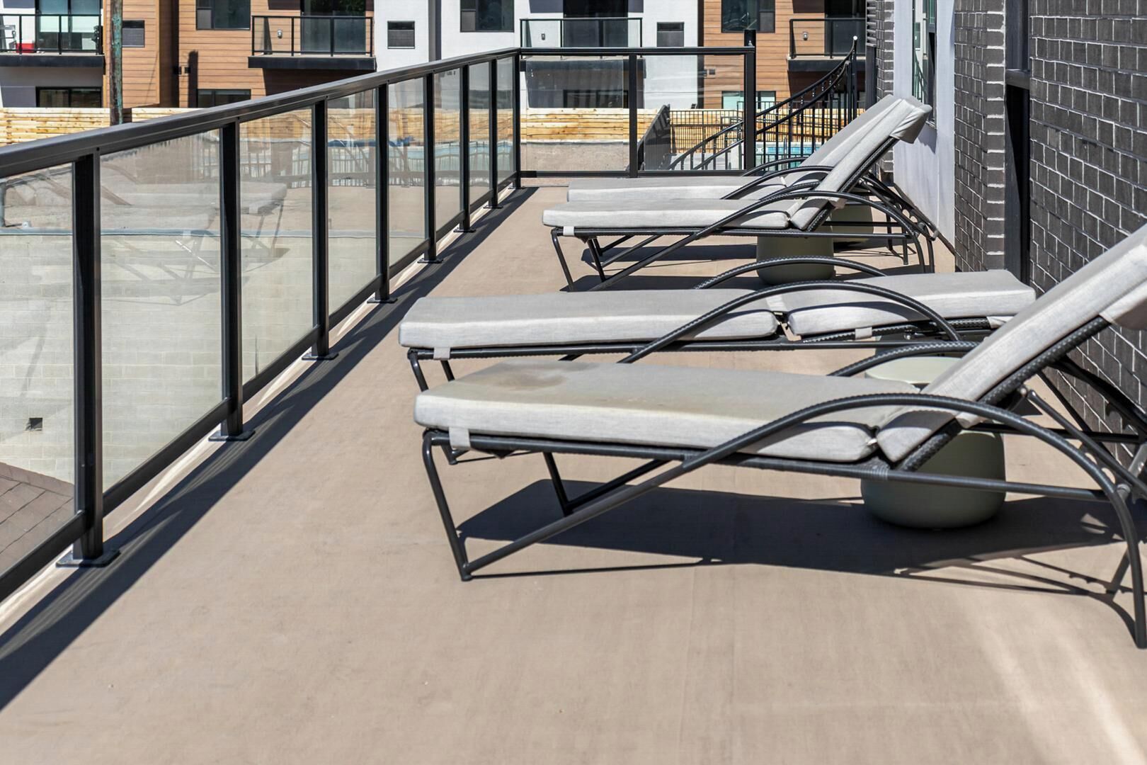 Terraza en la azotea con sillones de sol y barandilla de cristal con vistas a una obra.