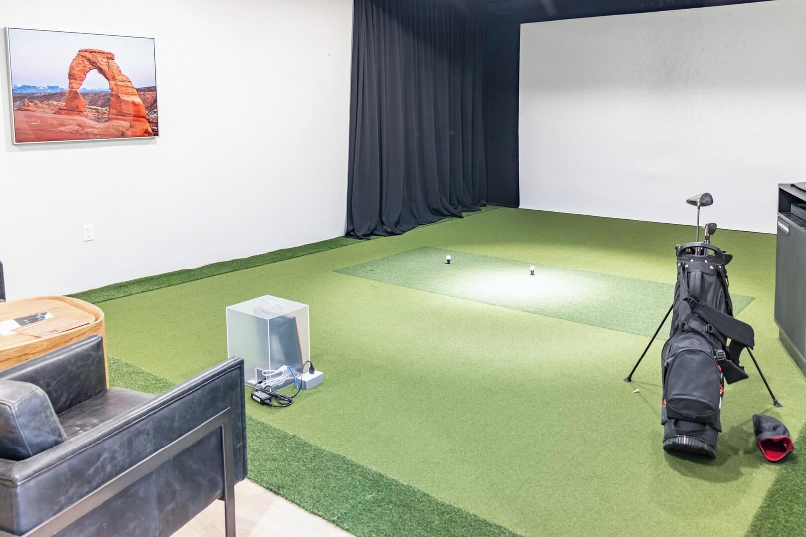 Ein Zimmer mit grünem Kunstrasenbelag, einer Golftasche, einer Projektionsleinwand und einem gerahmten Bild einer natürlichen Felsbrücke.