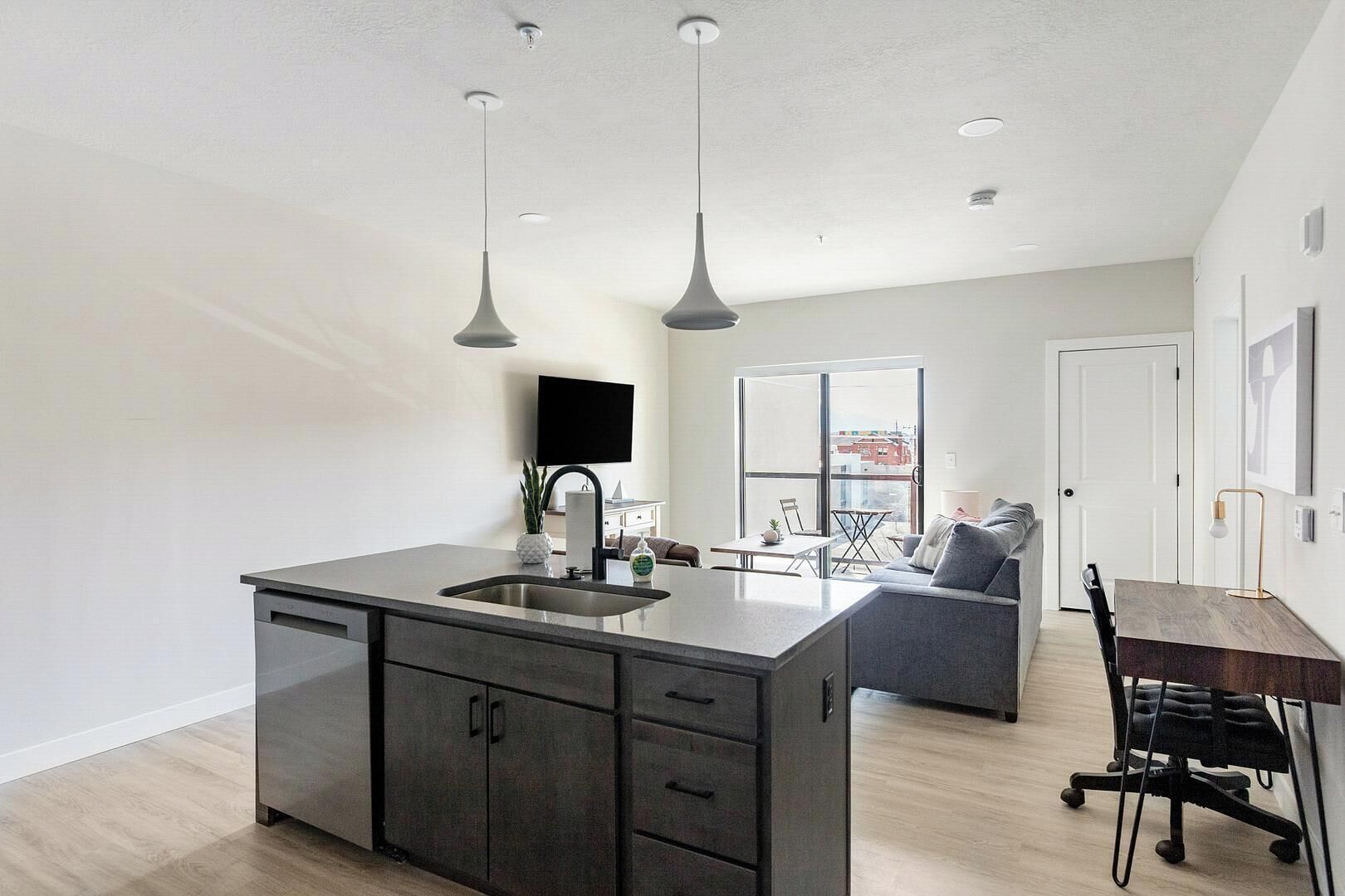 Een moderne keuken met een centraal eiland, een eethoek met tafel en stoelen, en een zithoek met een bank en televisie.