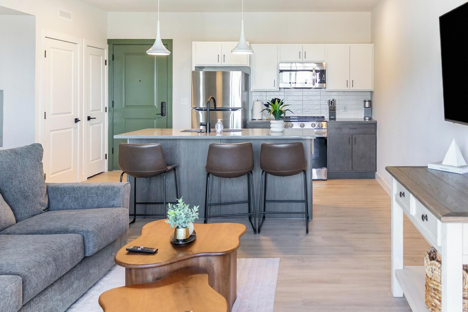 A modern kitchen with a central island, bar stools, and a dining area with a sofa and coffee table.