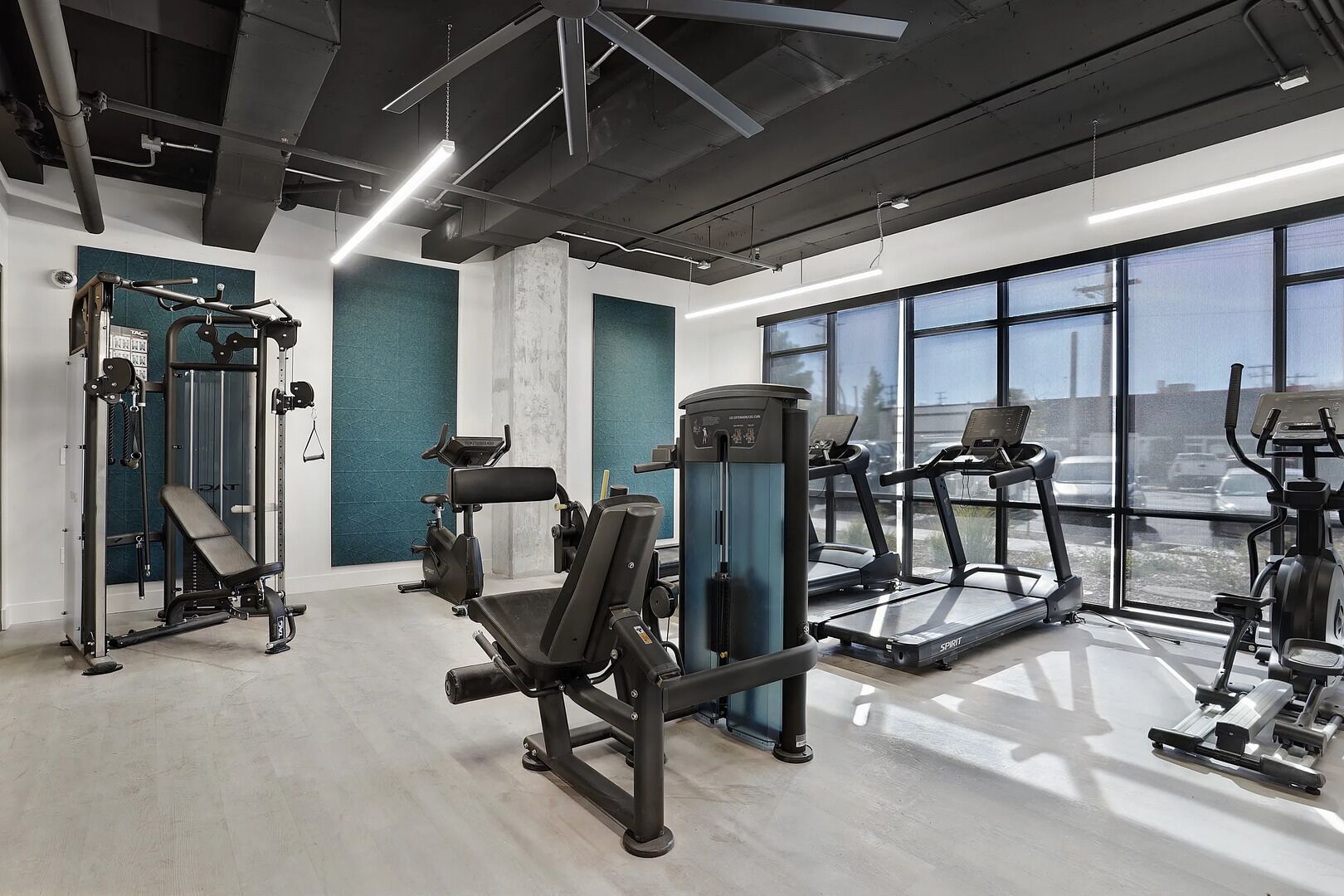 A gym with various exercise equipment, large windows, and a concrete floor.