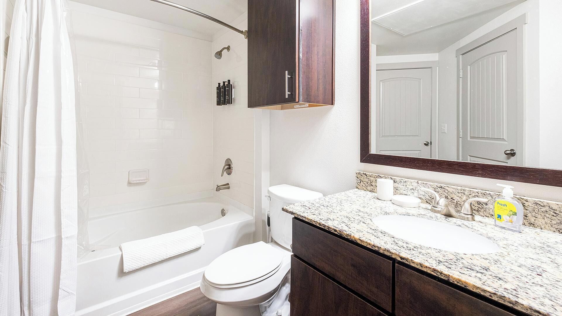 A bathroom with a bathtub, toilet, vanity with a mirror, and a shower curtain.