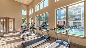Et fitnessrum med løbebånd, motionscykler og udsigt til en pool.