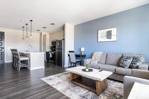 A modern living room with a sofa, coffee table, and a dining area with chairs. - Landing | Incredible 1BD, Pool, Gym (Indianapolis)