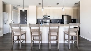 Une cuisine moderne avec des meubles en bois, un îlot central doté de tabourets de bar, un éclairage suspendu et un réfrigérateur en acier inoxydable.