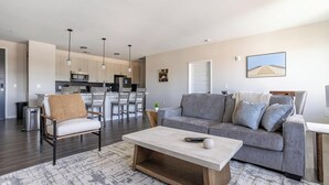 A modern living room with a grey sofa, a wooden coffee table, and a dining area with a kitchen in the background. - Landing | Modern 2BD, Pool, Gym (Indianapolis)