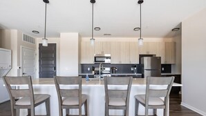 A modern kitchen with a central island, pendant lighting, and wooden chairs. - Landing | Modern 2BD, Pool, Gym (Indianapolis)