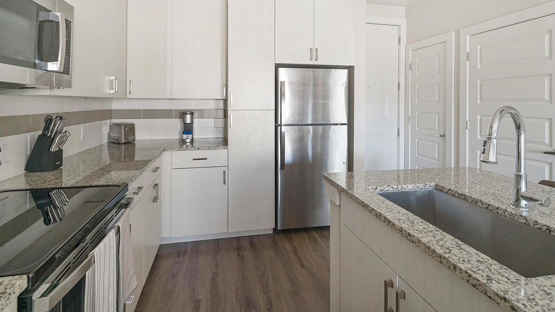 A modern kitchen with white cabinets, a stainless steel refrigerator, a microwave, and a granite countertop.