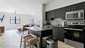 Eine moderne Küche mit einer zentralen Kochinsel, Edelstahlgeräten und einem Essbereich mit Sofa und Stühlen.