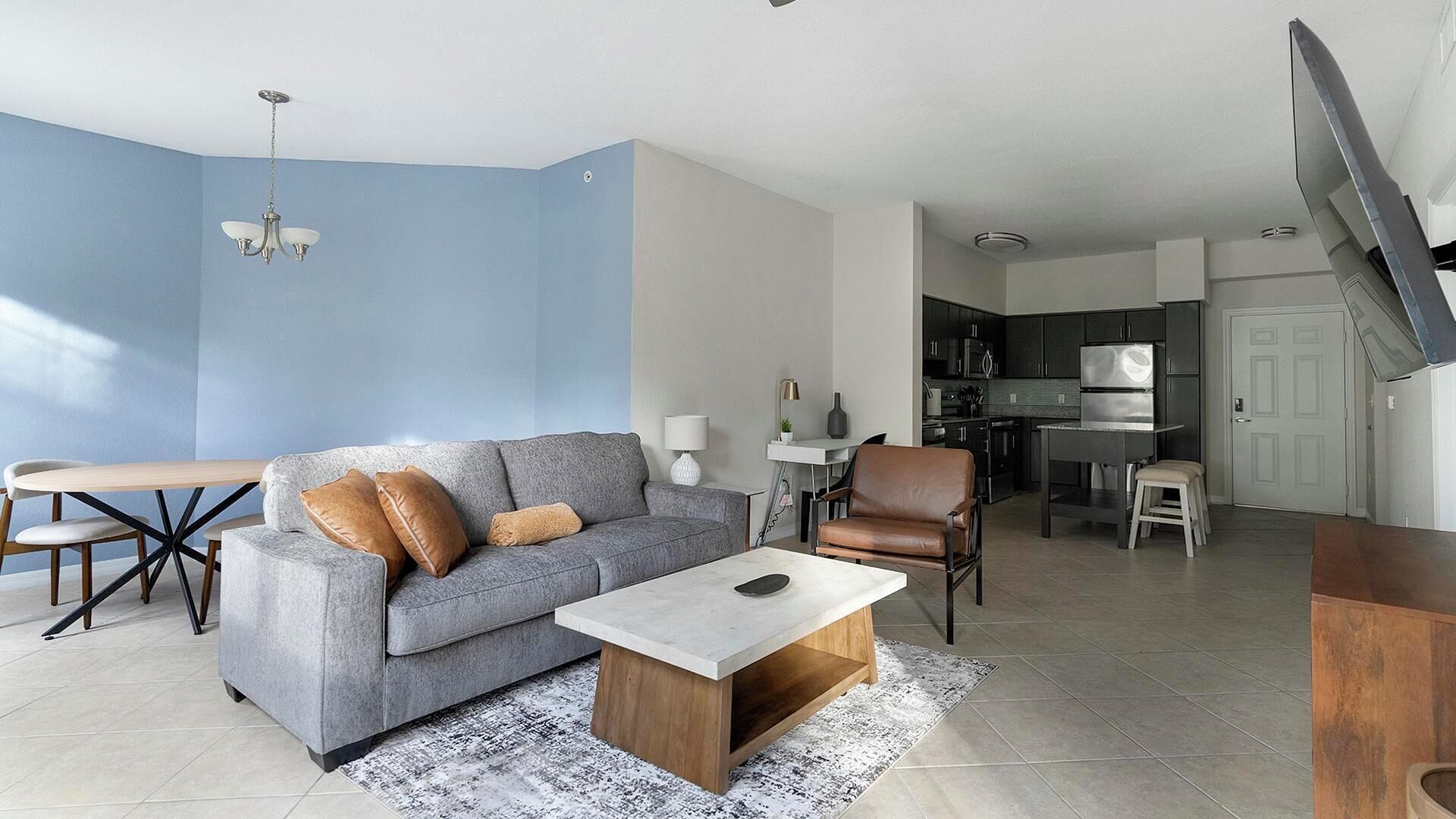 Uma sala de estar moderna com um sofá cinzento, uma mesa de centro de madeira e um espaço de jantar com mesa e cadeiras.