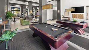 Ein Billardtisch in einer modernen Lobby mit Barbereich, Sitzgelegenheiten und einem großen Fenster.